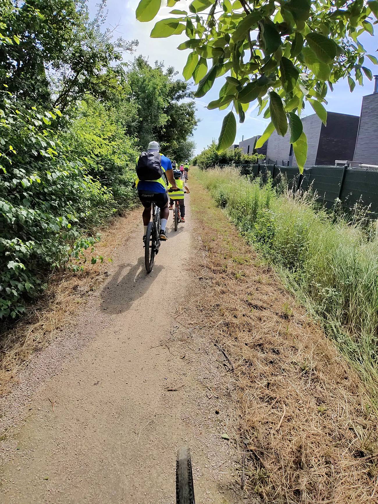 Groupe de cyclistes en gilets jaunes sur un chemin de terre bordé de verdure à Pusignan, pendant la sortie Puz à Vélo